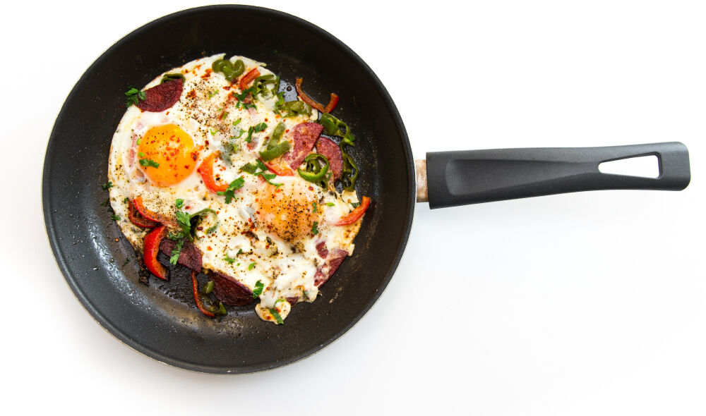 Fried eggs with veggies in skillet.